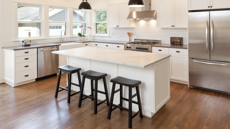 L-shaped kitchen with wood floors, white cabinets, stainless steel appliances, and an island with three black counter stools