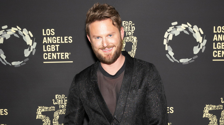 Bobby Berk smiling wearing a sparkly black tuxedo and a brown tshirt at a Los Angeles LGBT Center event