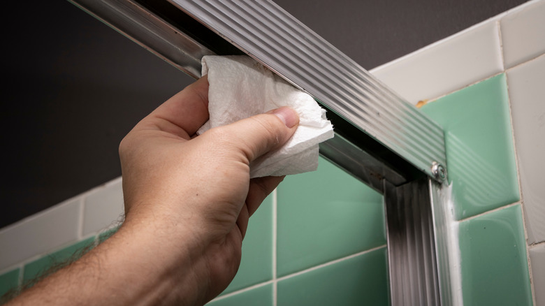 hand cleaning shower tracks with a paper towel