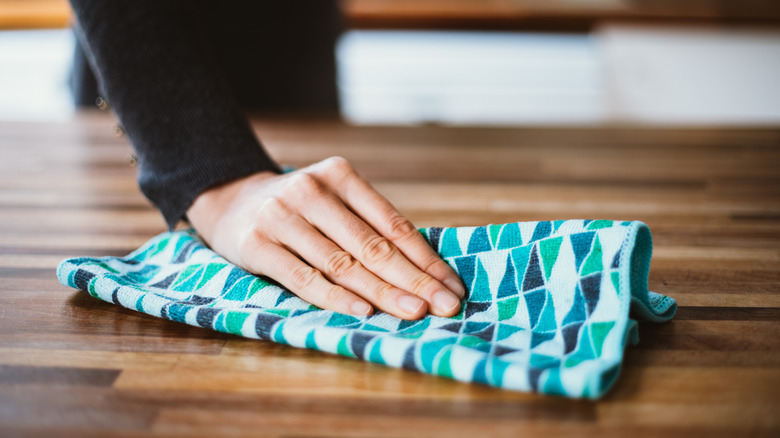 woman's hand with dish towel on wooden countertop