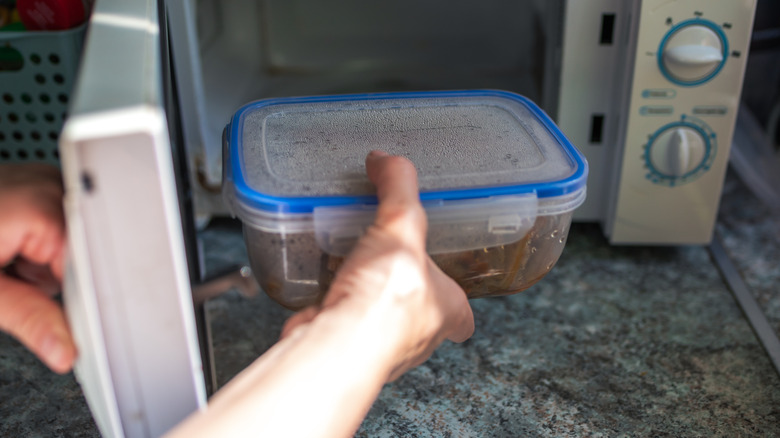 hand putting plastic container in the microwave