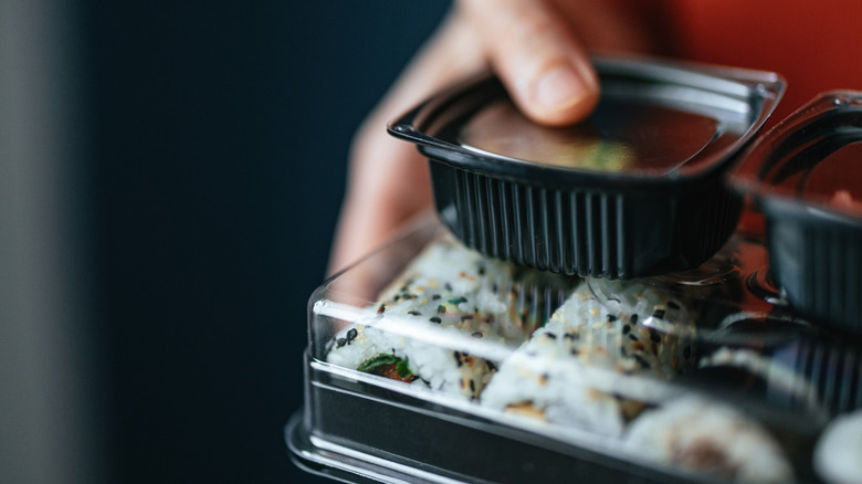 person's hand carrying takeout sushi in black plastic containers with clear lids