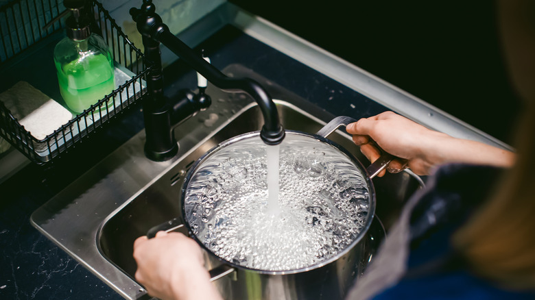 woman filling large pot with tap water in sink