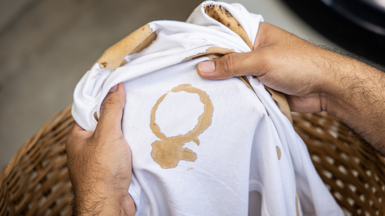 Hands holding a white shirt with coffee stains