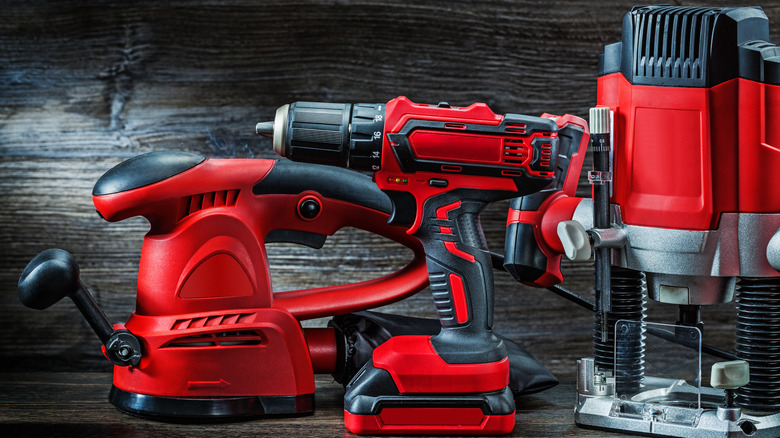 collection of red and black corded and cordless power tools against a dark wooden background