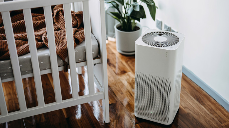 air purifier sitting in the corner of a room next to a crib and plant