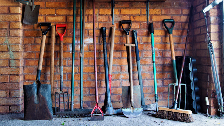 an assortment of yard tools leaning haphazardly against a brick wall of a garage