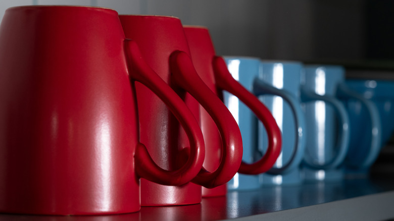 Close up of a neat row of mugs in a kitchen cabinet. Three red upside-down mugs are in focus, and 3 blue mugs are in the background.