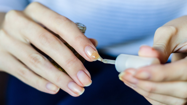 Close up of a woman applying clear nail polish to one of her hands.