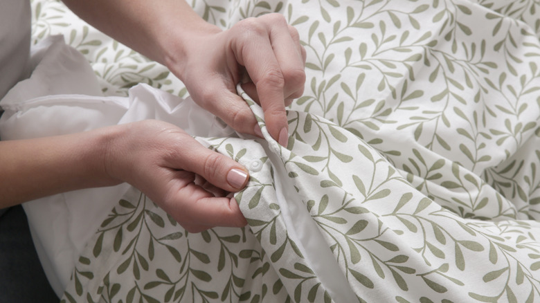 person snapping a green leaf printed duvet over a white duvet insert