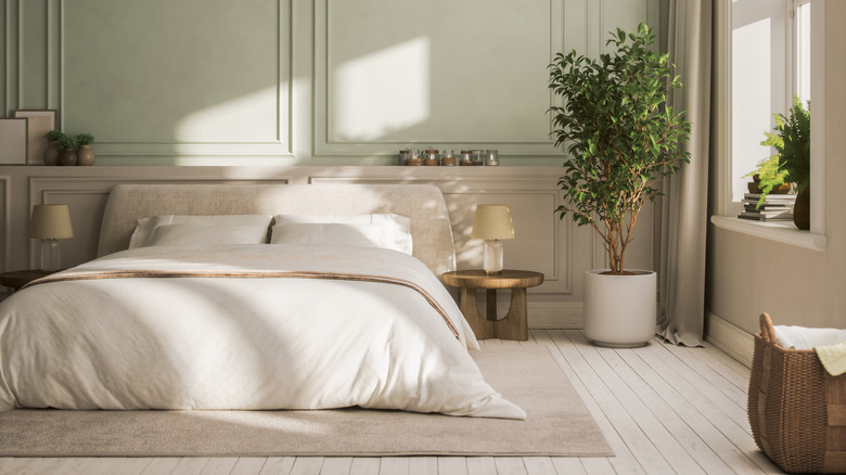 bedroom with cream bedding, sage green walls, cream wainscoting, and painted cream wood floors