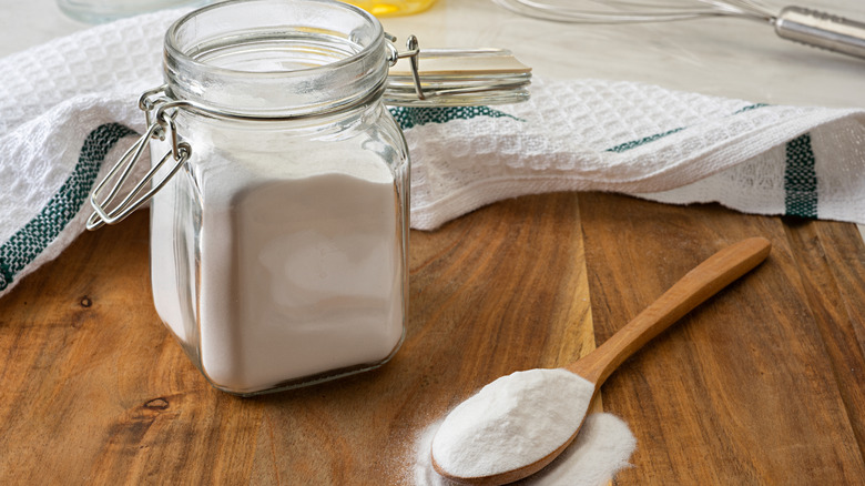 Open jar of baking soda and wooden spoon