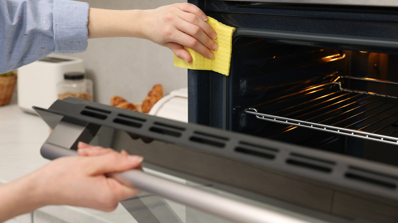 Hand with a yellow rag wiping an oven clean