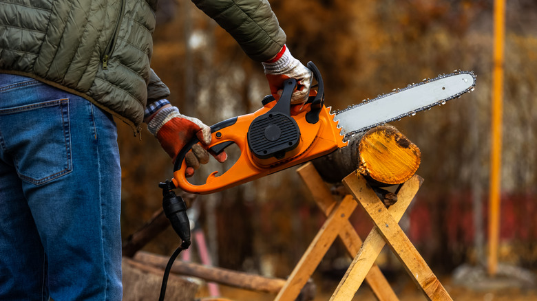 A man uses an electric chainsaw to cut a piece of wood