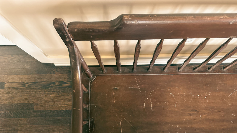 An old wooden bench covered in scratches, The camera is looking down on the bench and the wood flooring below.