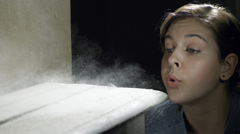 Woman blowing dust off a shelf