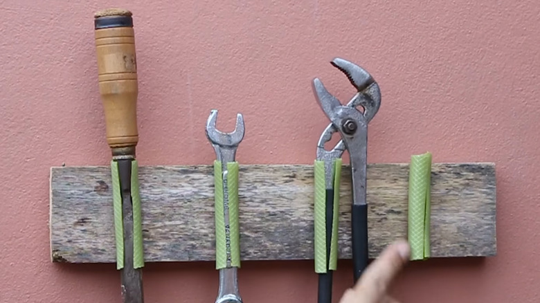 Tool holder made from old board and split pieces of garden hose