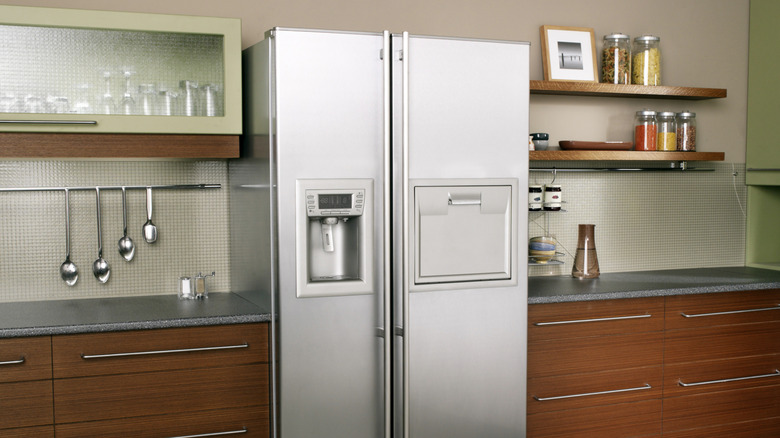 A stainless steel refrigerator standing in kitchen between wooden cabinets