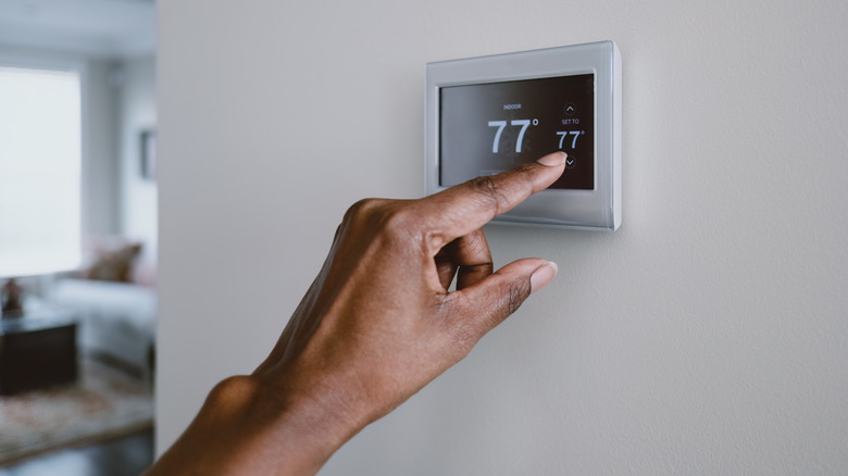 Close up on a black female's hand adjusting the thermostat in a home.