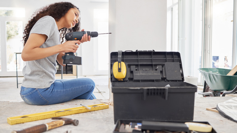 woman with power drill, tools, and toolbox working on wall