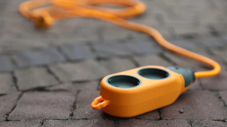 A close-up photo of an orange outdoor extension cord sitting on pavement.