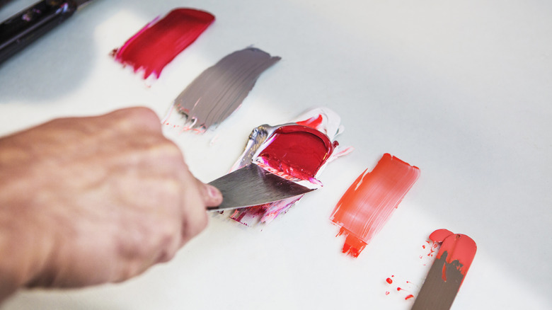 person painting shades of red and gray onto a white surface