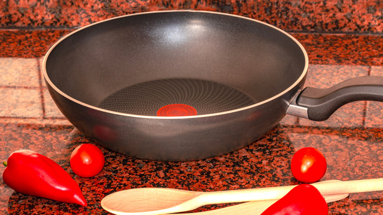 A pan and red peppers on top of a red granite countertop