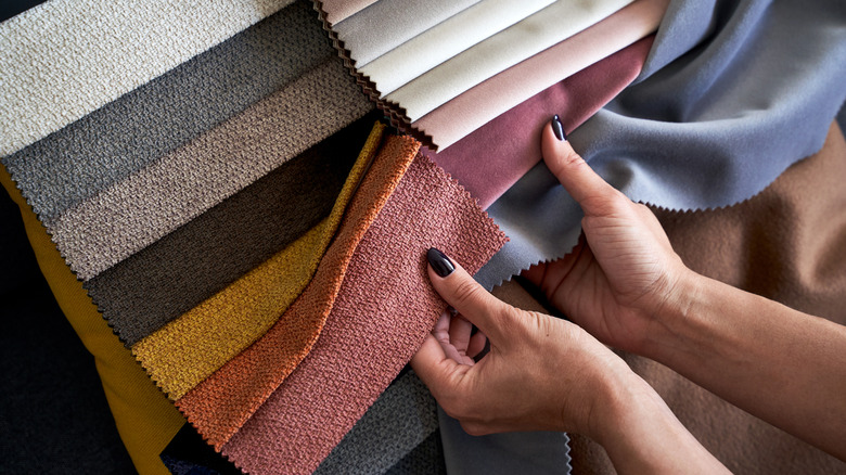 A woman's hands holding various fabric samples for upholstery in various colors and textures