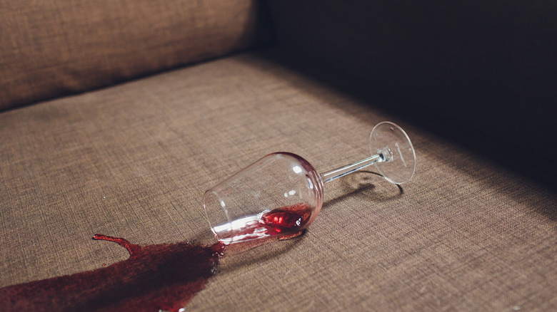 A glass of red wine tipped over and spilled onto gray tweed sofa