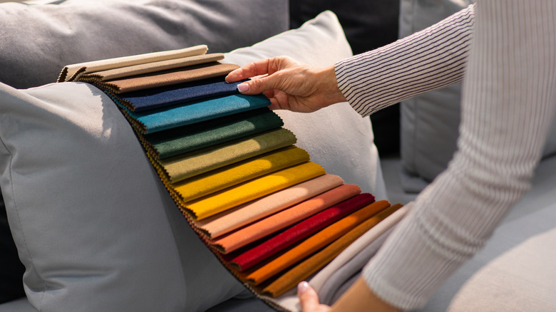 woman holding up colorful velvet upholstery fabric samples to a gray sofa cushion