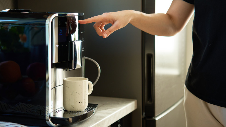 close up of a hand pressing a button on a coffee maker with a mug in place for brewing