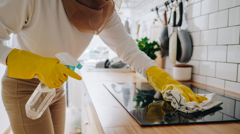 woman spraying clear liquid onto glass cook top