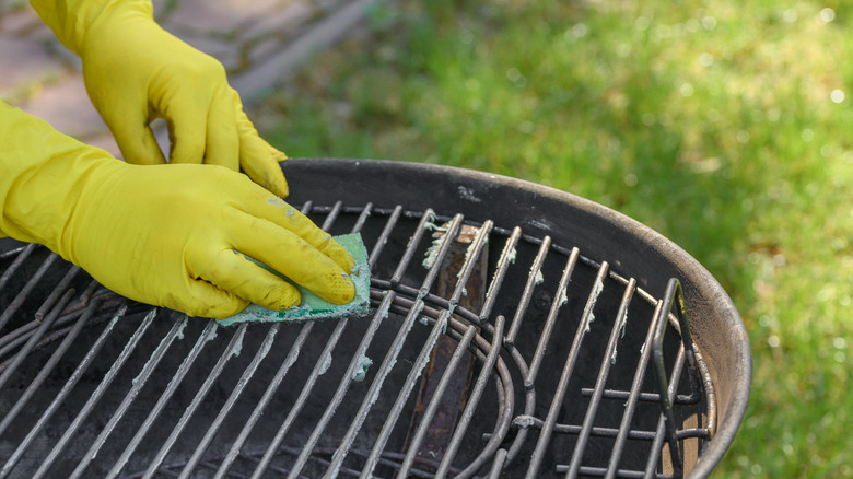 a dirty and filthy grill grate being cleaned by someone with yellow rubber gloves