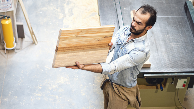 man looking  at a solid piece of wood in a workshop as he creates a cutting board