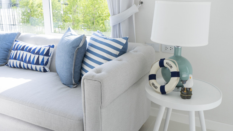 Close-up of a couch and end table in a mostly white living room punctuated by nautical accents