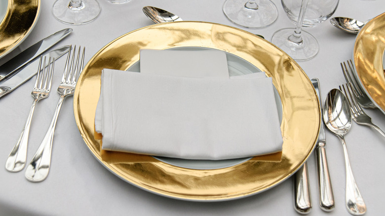 a very formal table setting with multiple glasses, forks, plates, gold rimmed plates and silverware