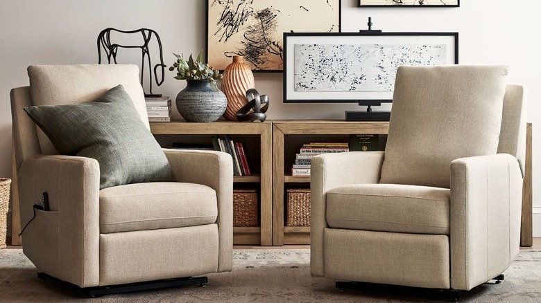 pair of modern cream power lift recliners in front of a bookshelf with decorative objects and art on top