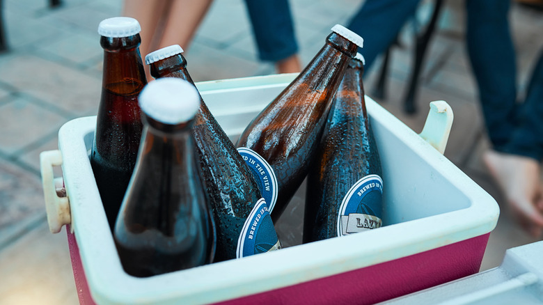 ice chest with beverages and ice, with people's legs in the background