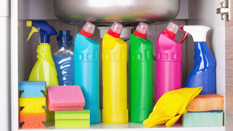 colorful cleaning supplies under a sink in a cabinet, such as bottles, spray bottles, sponges, and gloves