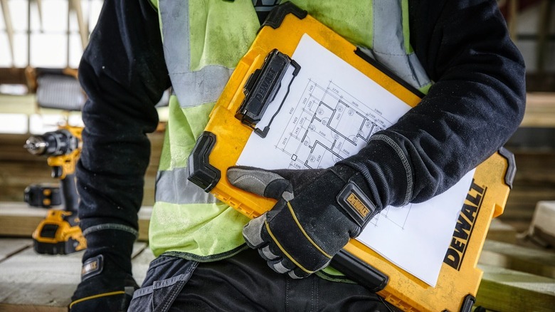 Man in construction site gear holding DeWalt clipbaord