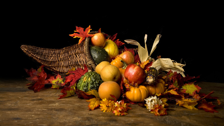 cornucopia on a table, filled with leaves, apples, squashes, and pumpkins