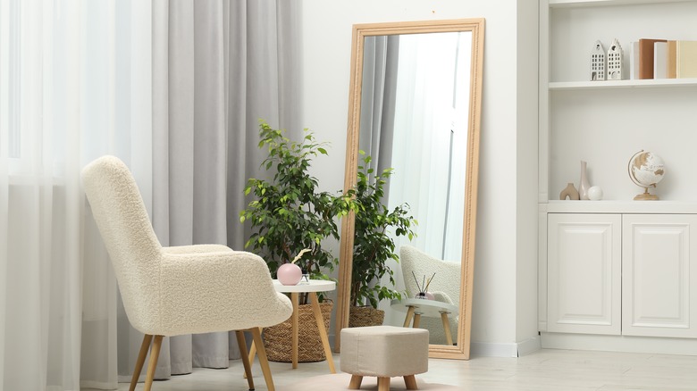 white room with a white MCM chair, table, gray ottoman, houseplant in front of a large mirror