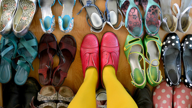 person with yellow tights and red shoes standing amidst pairs of other shoes, mostly heels