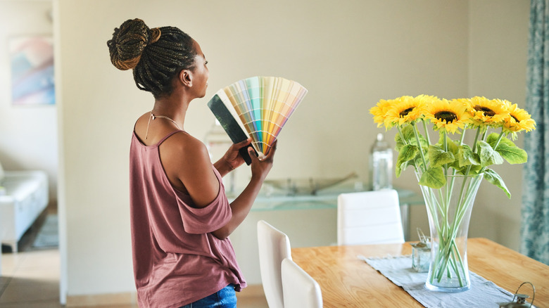 woman standing in her dining room with a paint deck fanned open to choose a paint color for the walls