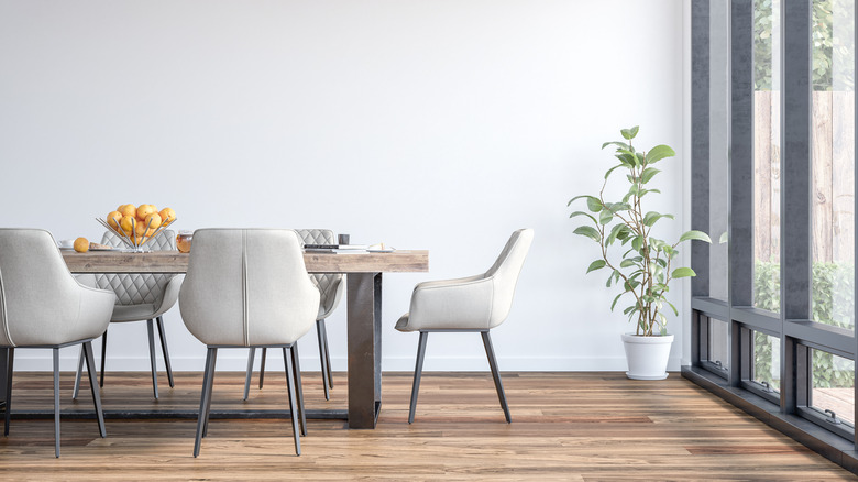 Dining room with white walls, wood table, and white leather dining chairs by a full-height black window