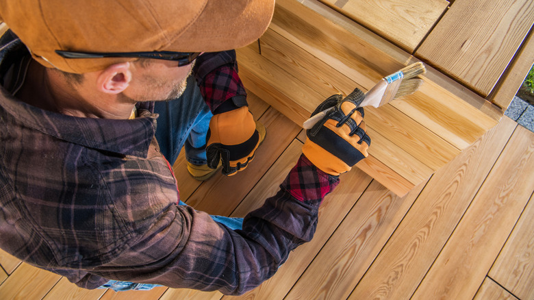 man in ball cap finishing outdoor furniture with brush