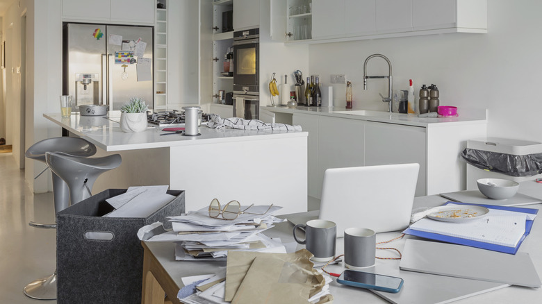 kitchen with piles of papers on the dining table, as well as clutter and dirty dishes scattered throughout