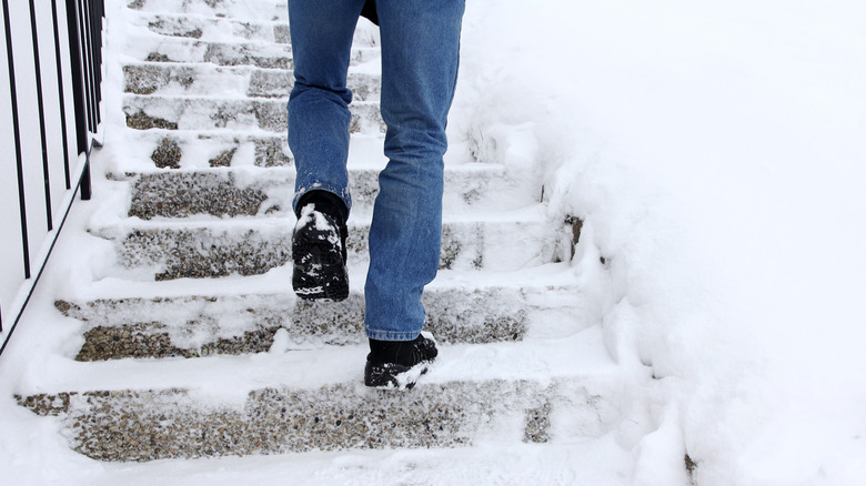 A man in jeans and black shoes walks up a slippery, snow-covered staircase.