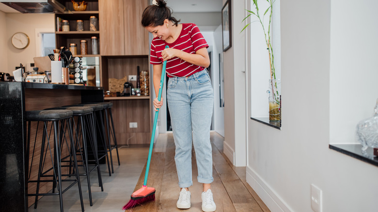 Young woman sweeping near barstools in home