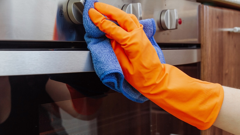 hand with an orange rubber glove using a blue microfiber cloth to clean a stainless steel range front